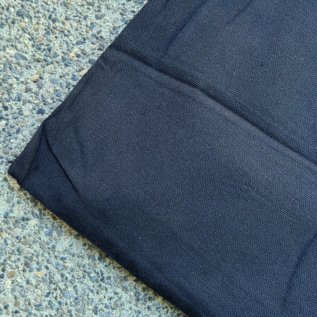 A close-up of a dark gray canvas bag laid diagonally on a textured concrete surface.
