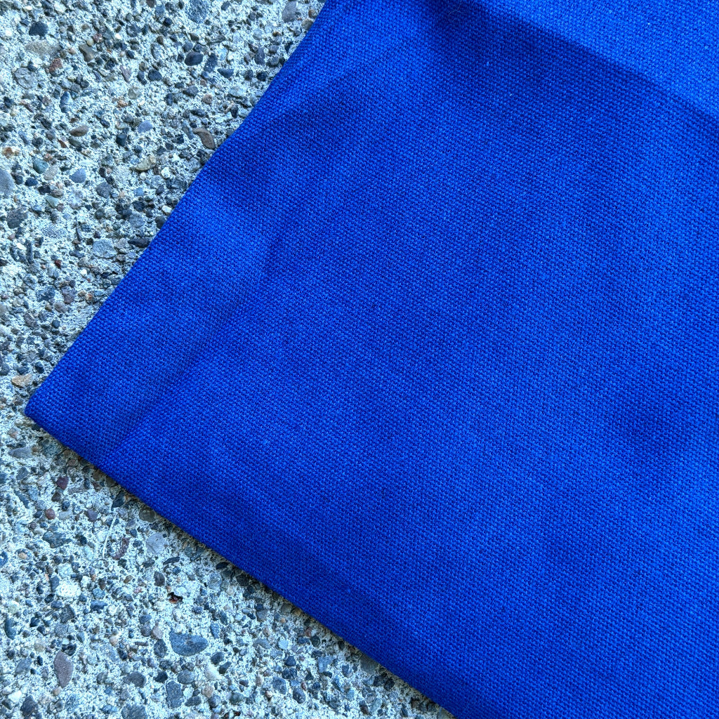 A close-up of a folded royal blue canvas bag, placed on a gray concrete surface.