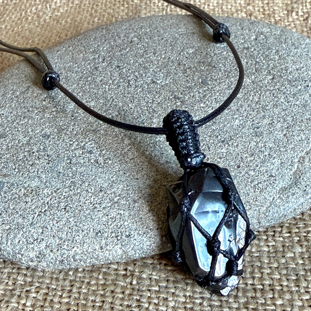 A black cord necklace with a black elite shungite pendant wrapped in black cord, displayed on a smooth gray stone over a burlap surface.