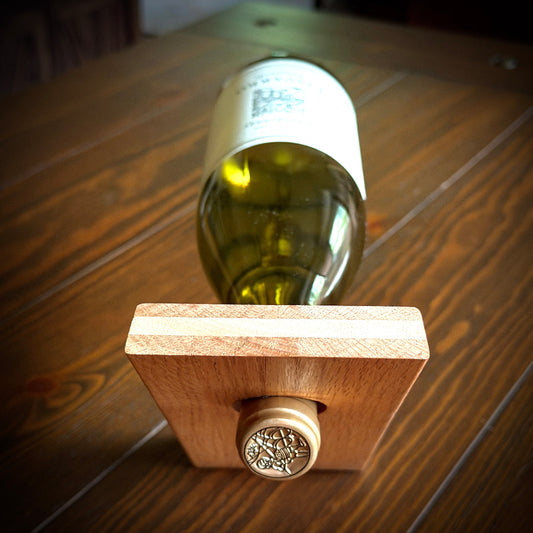 A wooden wine bottle holder, supporting a green glass wine bottle on a dark wooden tabletop.