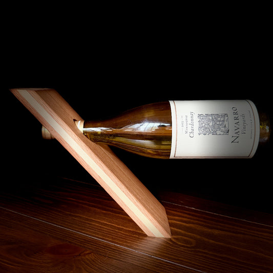 A wooden wine bottle holder cradling a bottle of Navarro Chardonnay against a solid black background, with the holder resting on a dark wood surface.