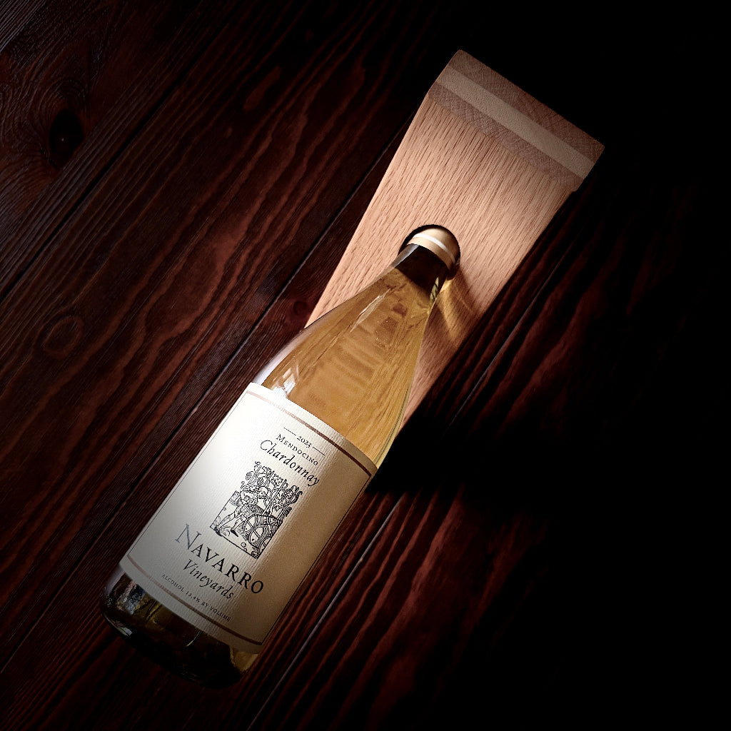 A bottle of Navarro Vineyard Chardonnay white wine in a gravity holder a dark wood surface next to a light wood block.