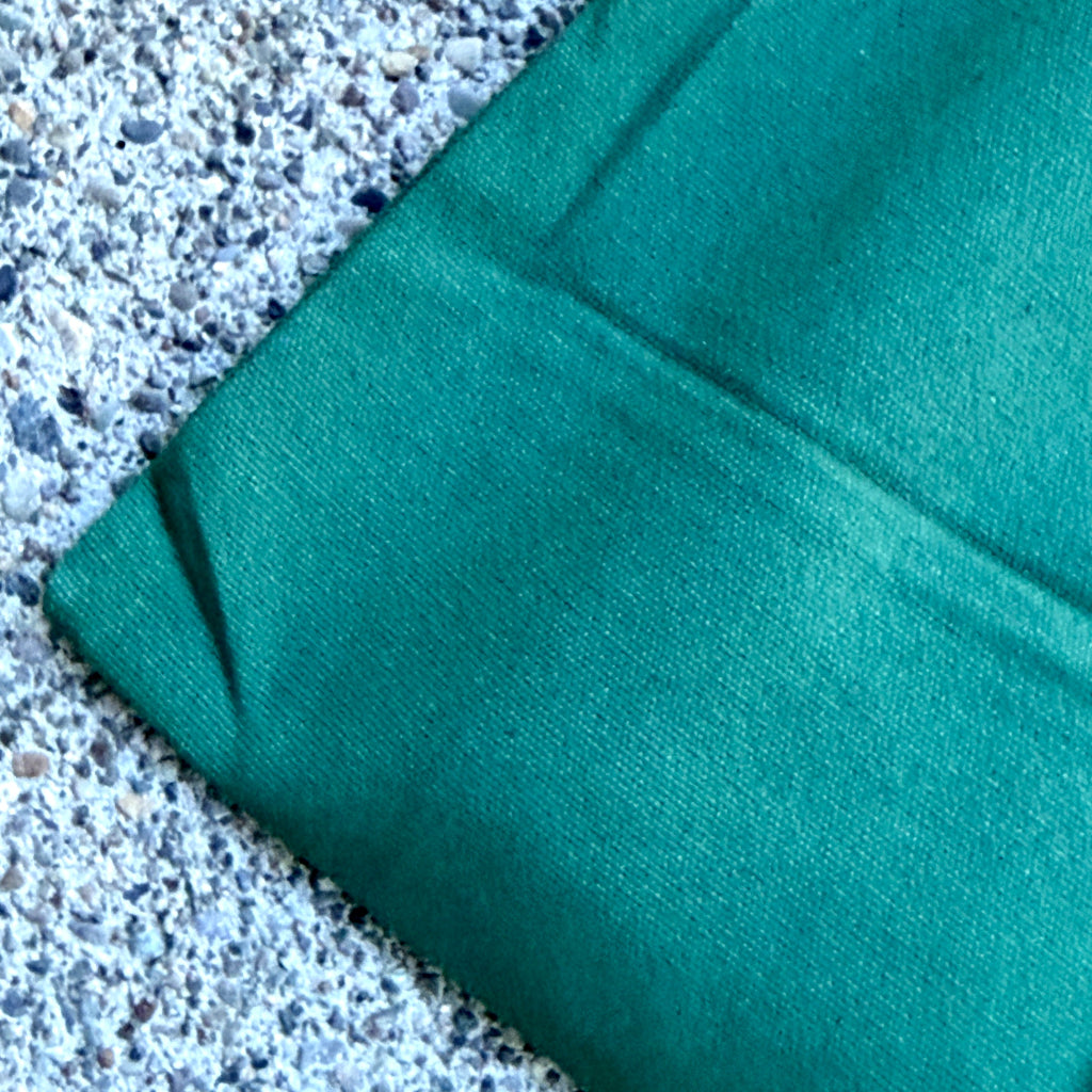 A close-up of a folded green canvas pouch, resting on a speckled concrete surface.