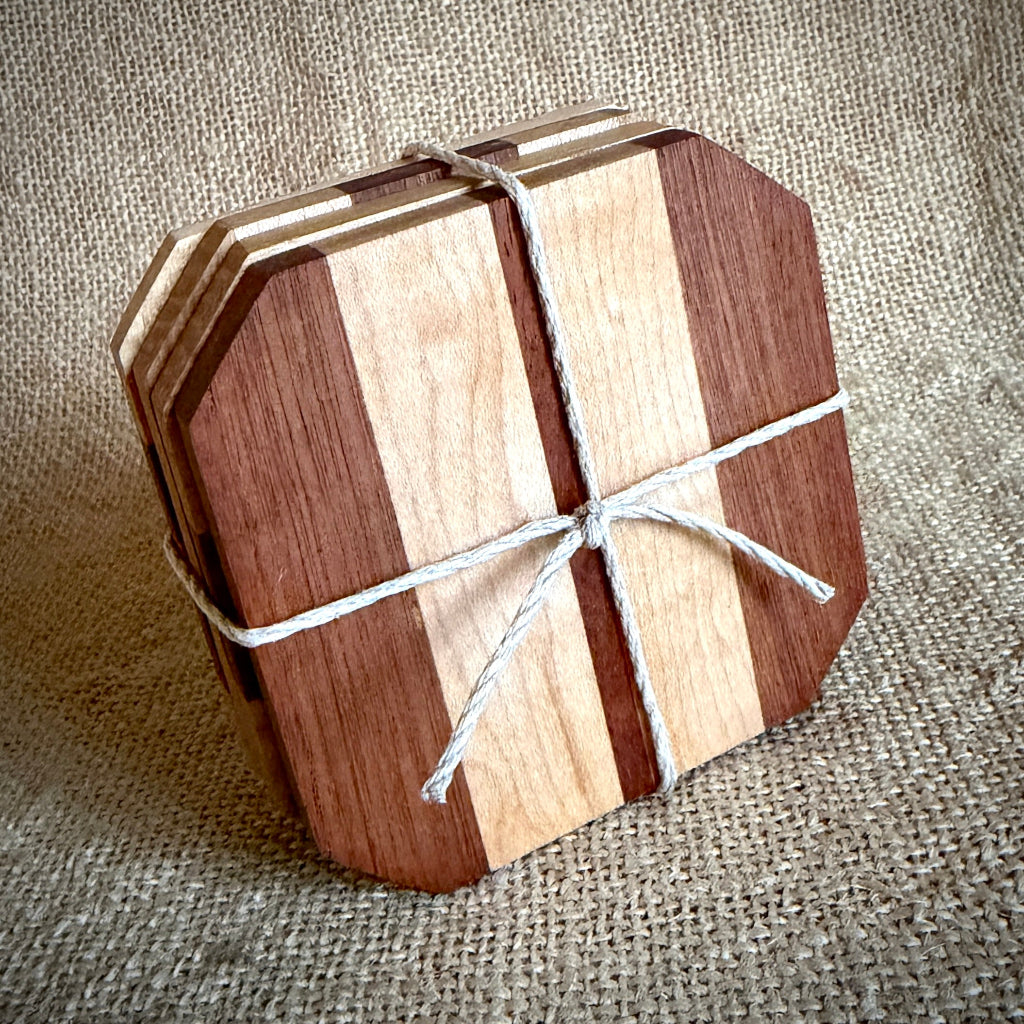 A set of four wooden coasters with alternating dark and light wood stripes, tied together with white twine on a textured burlap background.