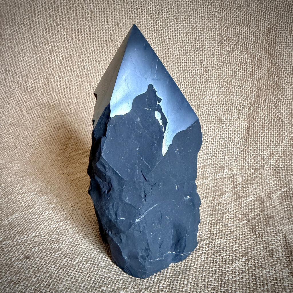 Large Raw Shungite Point standing up on table with burlap cover