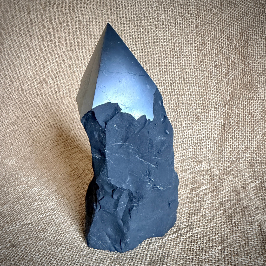 Large Raw Shungite Point standing on table with natural fiber cover