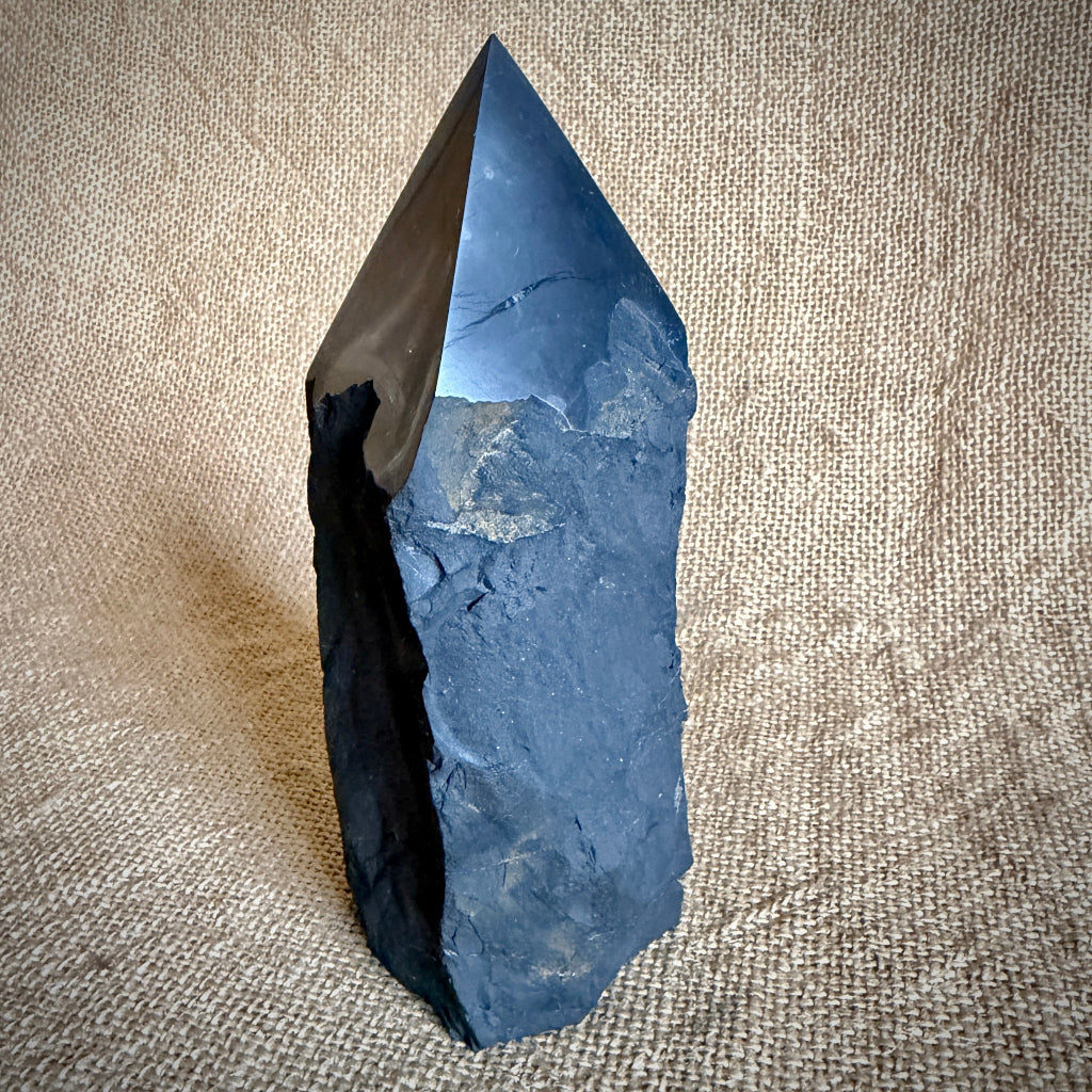 Large Raw Shungite Point upright on table with natural fiber background 