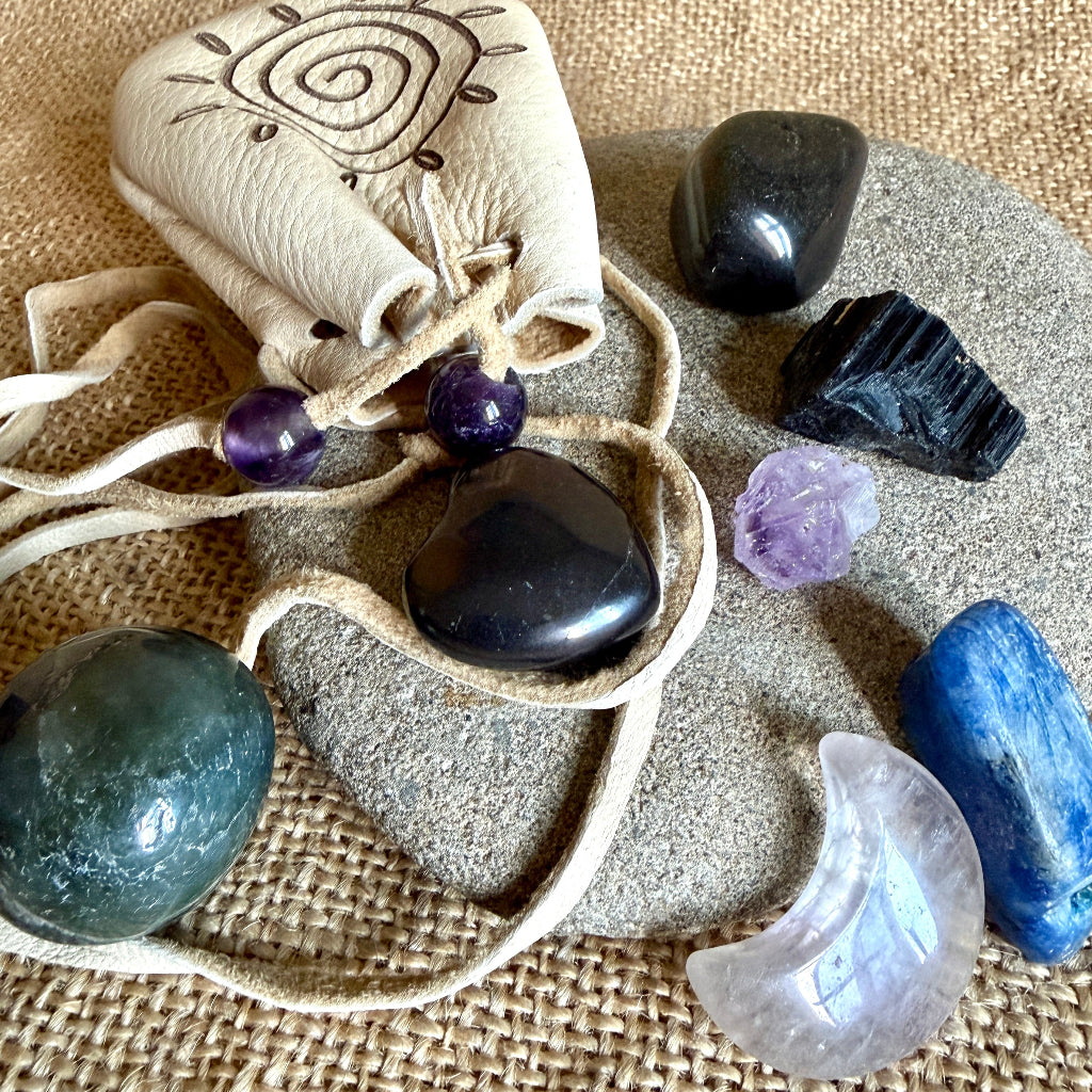 A leather drawstring pouch with a sun motif, surrounded by polished and raw crystals on a burlap background.