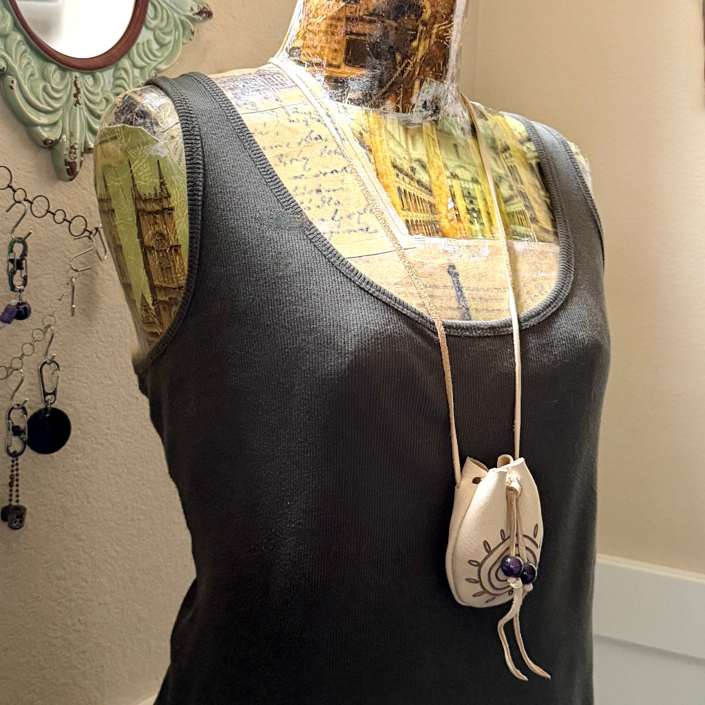 A black ribbed tank top displayed on a vintage-style mannequin torso, featuring a cream-colored drawstring pouch necklace with a blue and white eye design hanging from a thin cord.