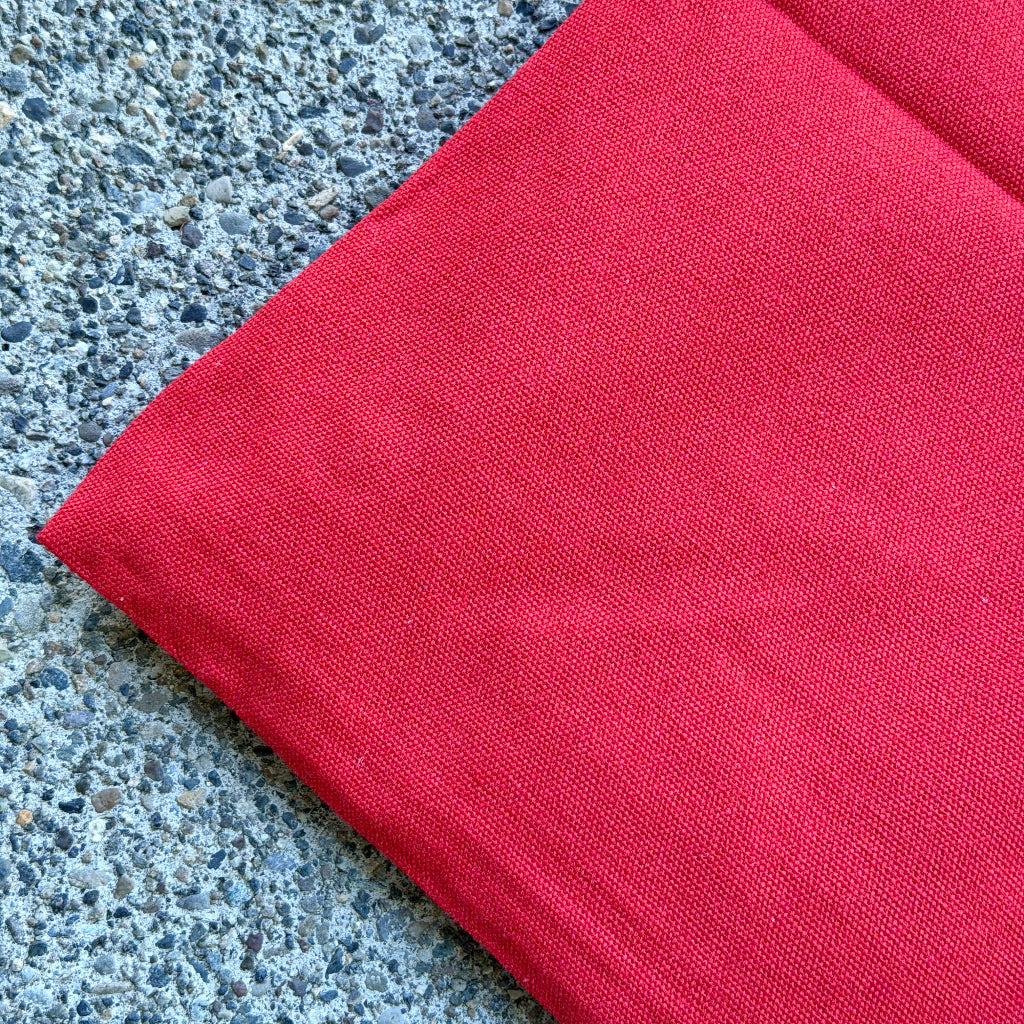 A close-up of a folded bright red canvas bag laid diagonally on a textured gray concrete surface.