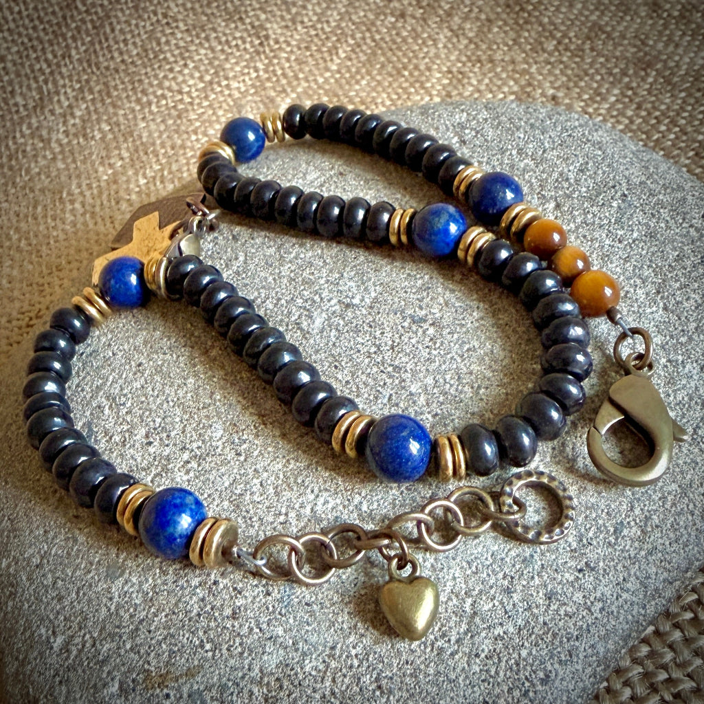 Rosary bracelet displayed on a textured gray stone surface, features shungite beads, bright blue lapis lazuli beads, and small bronze spacer rings.